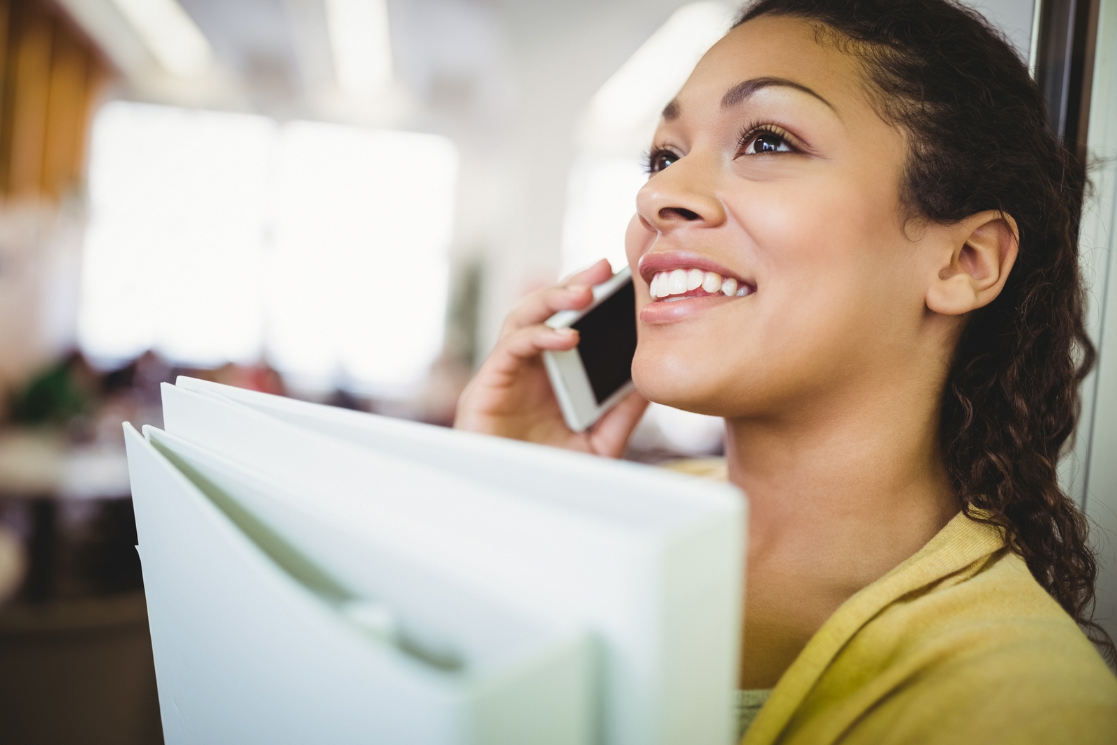 Eine Frau mit einem Aktenordner im Arm spricht lächelnd in ein Telefon